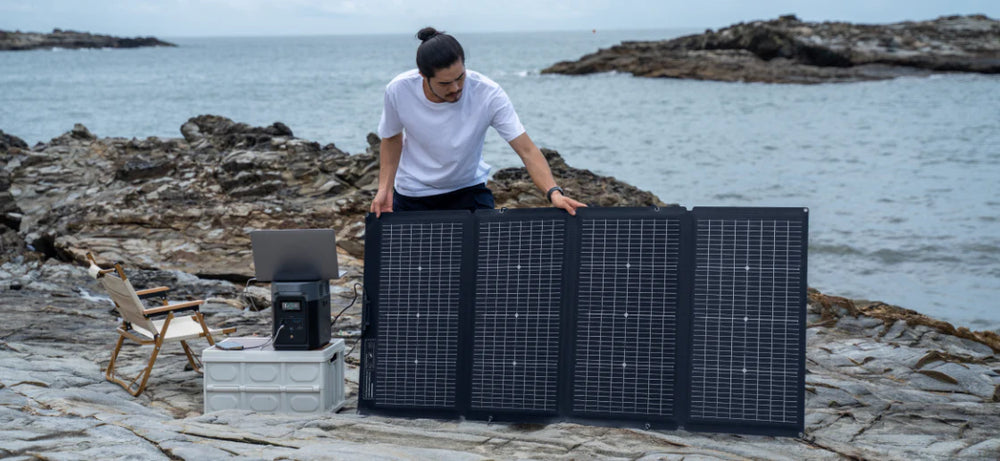 A man sets up an EcoFlow solar panel beside an Delta 2 Portable Power Station, with the ocean behind.