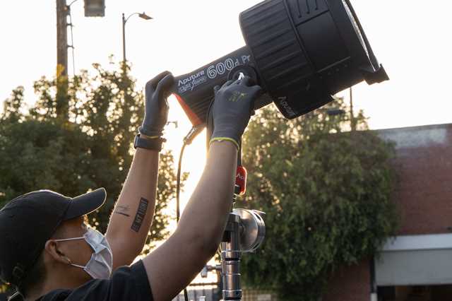 An image showing a lighting technician adjusting the yoke on an Aputure 600d Pro with an Aputure F10 Fresnel mounted to it.