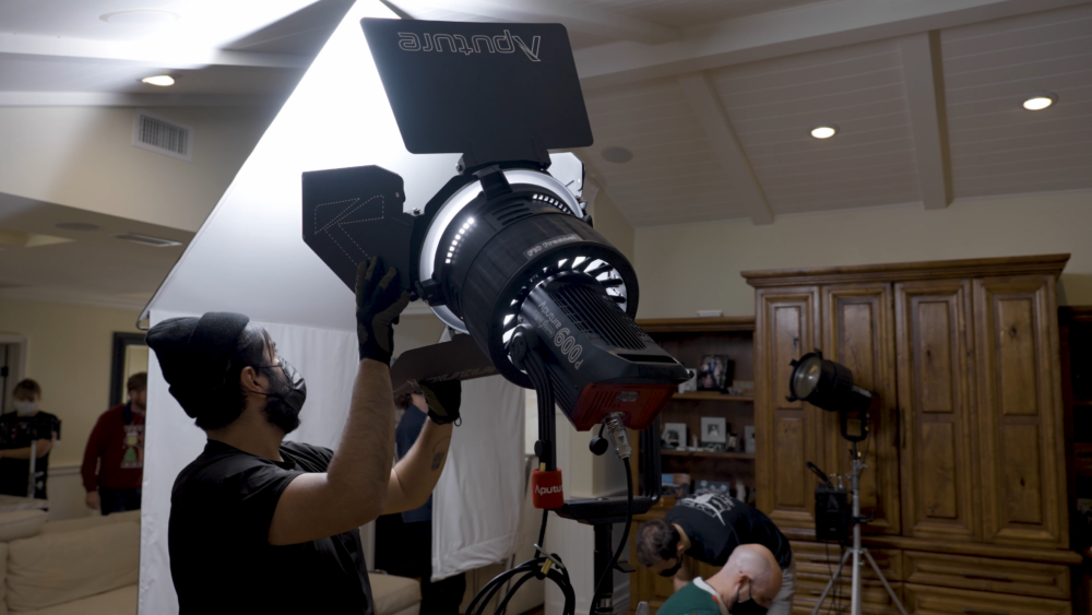 An image of a lighting technician spreading a set of Aputure F10 barndoors attached to an Aputure F10 fresnel to cover more area on a bounce.