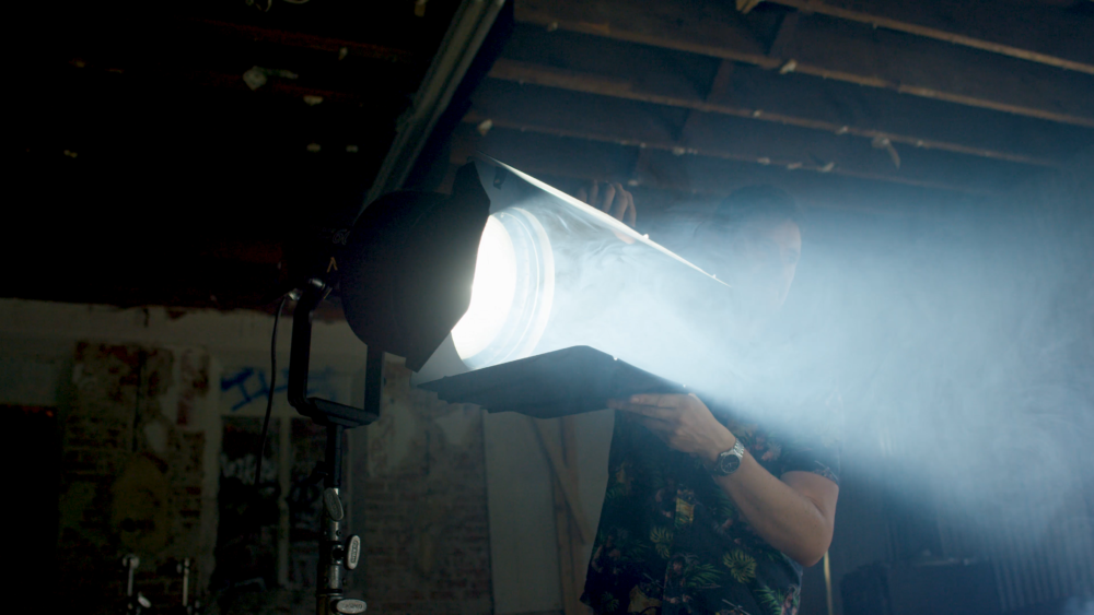 An image of a lighting technician adjusting the barndoors on a set of Aputure F10 barndoors attached to an Aputure F10 fresnel.